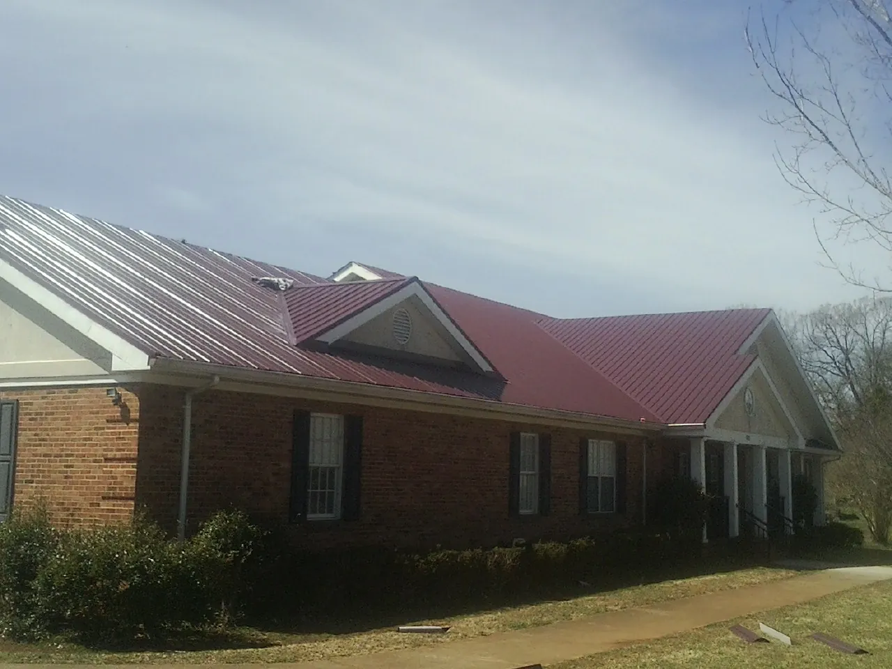 Red metal roof with gabled entries on a long brick building, from a Hail Damage Roof Repair job in Cortland