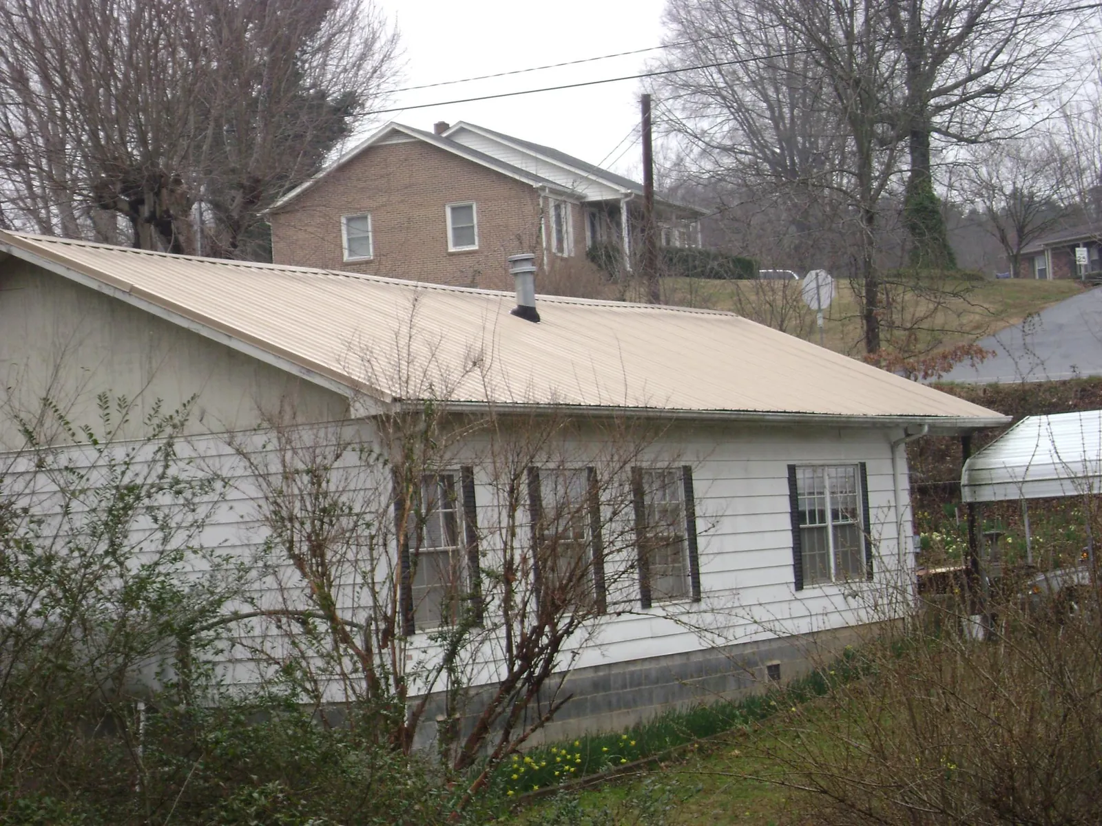 Tan metal roof on a white sided house set into a hillside — Commercial Roofing by Roofing Brothers in Cortland
