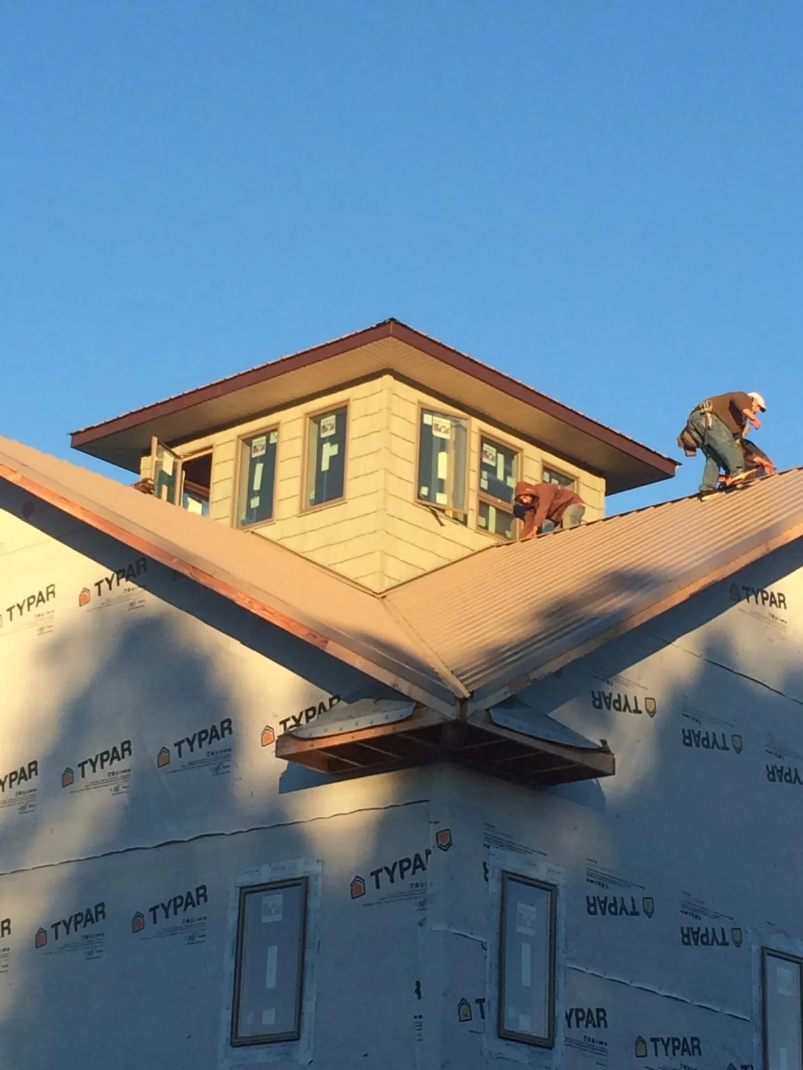 Roofers working around a rooftop cupola on a new metal roof at sunset — Roof Waterproofing in Cortland by Roofing Brothers